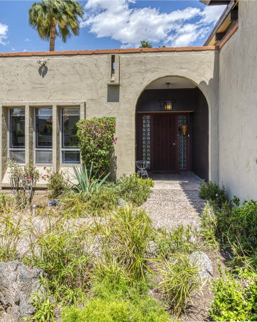 Front entry of 1542 E Solano Dr, Phoenix: a stucco home with an arched doorway, desert landscaping and a palm tree
